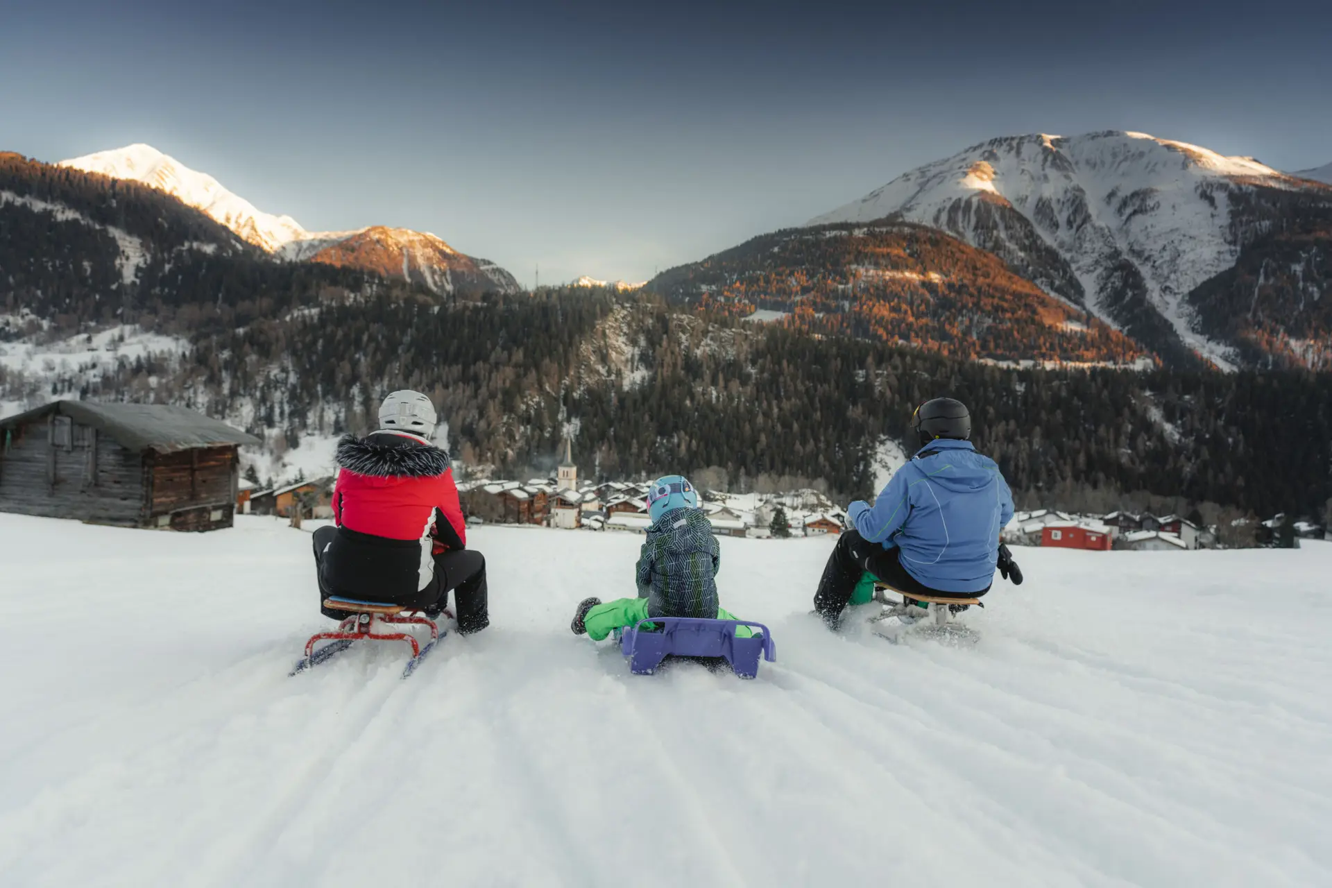Gezin rodelt in de sneeuw met uitzicht op het dorp en de bergen van de Aletsch Arena, Wallis